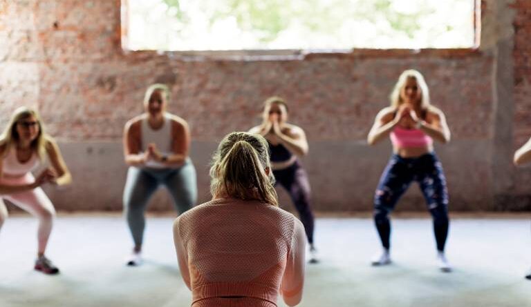 back view of female trainer giving exercise class to female sports team indoors