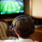 Back view of a boy wearing headphones and looking at a TV screen.